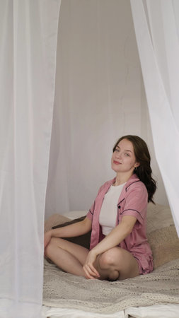 A young woman stretches on her bed surrounded by soft, white curtains. This image captures the essence of morning rituals, promoting self-care and the importance of a healthy start to the day.の写真素材