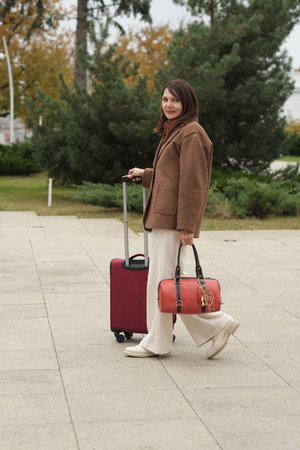 A traveler with a red suitcase and a matching handbag outdoors on a calm autumn day. This symbolizes solo journeys and the freedom to explore new places.の写真素材