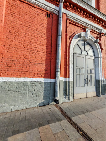 A sturdy metal downspout attached to a textured red brick facade with white window trims. The photo captures construction materials and the importance of drainage systems in urban buildings.の写真素材
