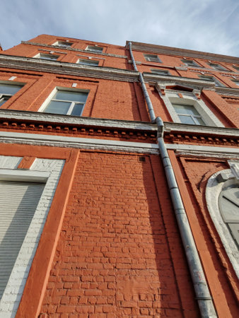 A close-up view of a red brick building with an industrial downspout system made of galvanized metal. The photo emphasizes material durability and installation precision.の写真素材