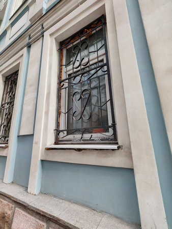 A close-up of a barred window with decorative ironwork, set in a pale blue and white facade.