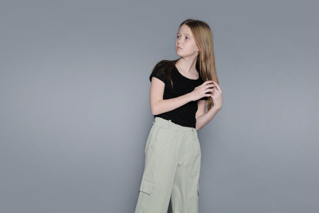 A girl stands holding her hair, looking thoughtfully to the side in a minimalist studio. Images like...