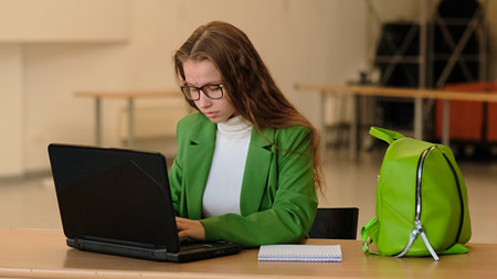 A focused schoolgirl works quietly on a laptop at a desk, warm indoor light and clean composition with copy space. This image connects to online study, screen time, and student wellbeing.の写真素材
