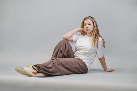 Seated and stretching her arms, a woman in casual attire including a white t-shirt and beige pants...