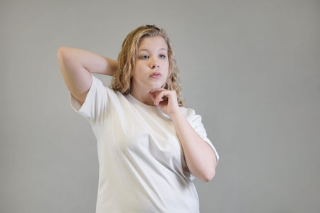 A young woman in a white t-shirt stretches her arms forward while seated against a neutral backdrop.