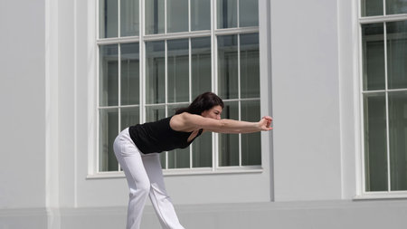 A woman performs a deep stretch, extending her arms forward to engage her core and back muscles. The...