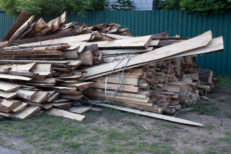 Old untreated building pile boards next to a fence. The wood has a rough texture. The grass is...