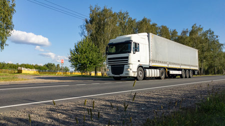 White semi-truck with a fully loaded cargo trailer driving along countryside road. The lorry travels on an empty freeway. Transport, cargo delivery conceptの写真素材