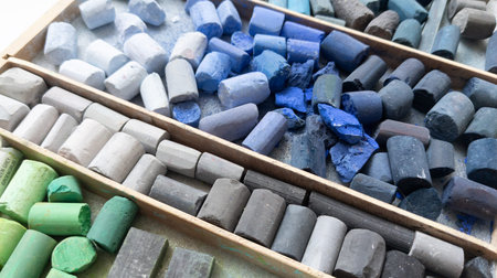 Collection of soft pastel crayons in dark blue, light blue, and gray in a wooden case for storing...