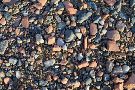 Texture of a rural road with sand, pebbles, and crushed stone. Natural gravel surface and geological background. Mixed granite stones on a coastal strip or dry riverbank.