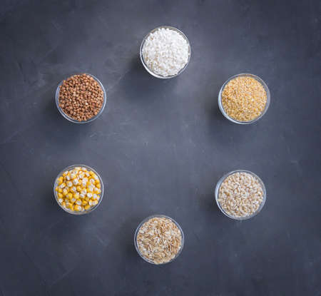 6 species of whole grains, in small containers, on a black background. Krupa are laid out in a circle, in the center of an empty place. Healthy food for vegetarians.の写真素材