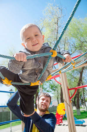 Dad, European in appearance, walks with his son on the playground. The child is happy to spend time with his father. The parent teaches the kid to play active gamesの写真素材