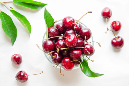 Ripe berry in a glass bowl, on a white background. Red cherries, in the center of the frame, are...