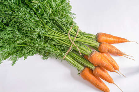 Carrots with a green tail on a light background. Fresh harvest of natural and healthy vegetables. Vitamin cocktail made of ripe carrots.の写真素材