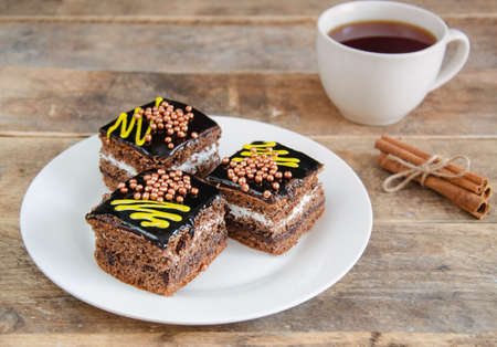Pieces of cake, in the center of the frame, a kettle of tea in the distance on a dark background. Sweets for hot drinks. Three pieces of chocolate cake on a white plate.の写真素材