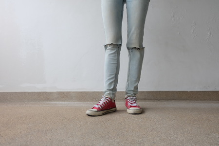 Young Fashion Woman's Legs in Blue Jeans and Red Sneakers on Floor Great For Any Use.の写真素材