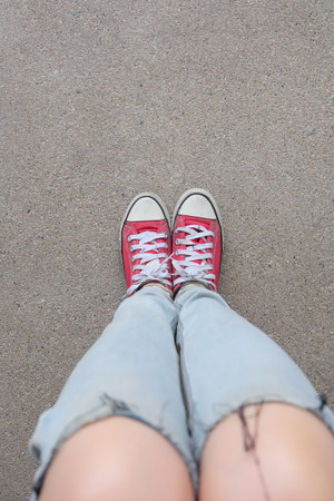 Young Fashion Woman's Legs in Blue Jeans and Red Sneakers on Floor Great For Any Use.