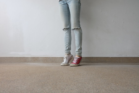 Young Fashion Woman's Legs in Blue Jeans and White, Red Sneakers on Floor Great For Any Use.の写真素材
