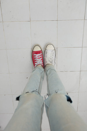 Young Fashion Woman's Legs in Blue Jeans and White, Red Sneakers on Floor Great For Any Use.