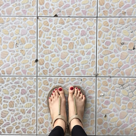 Female Legs Wearing Footwear Shoes or Flip-flop Outdoor Red Nail on Floor Background Great For Any Use.の写真素材