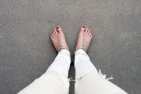 Selfie Feet Wearing Gold Sandals and White Jeans on Ground Background Great For Any Use.