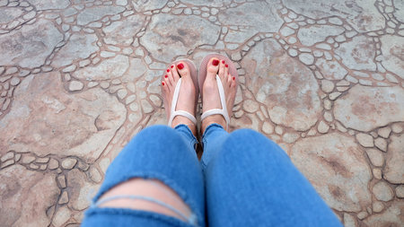 Close Up on Girl's Feet Wearing Sandals and Blue Jeans on The Tile Great For Any Use.