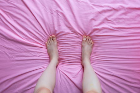 Close Up of Female Feet and Slim Legs on the Pink Bed, Feet in the Bedroom Background at Home Great For Any Use.の写真素材