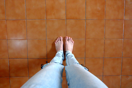 Close Up Woman Barefoot Wear Blue Jeans on Brown Tile Background Great For Any Use.の写真素材