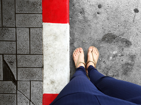 Female Feet Wear Sandals Standing Red and White Concrete Curb, Concrete Road - Sidewalk for Background Great For Any Use.の写真素材