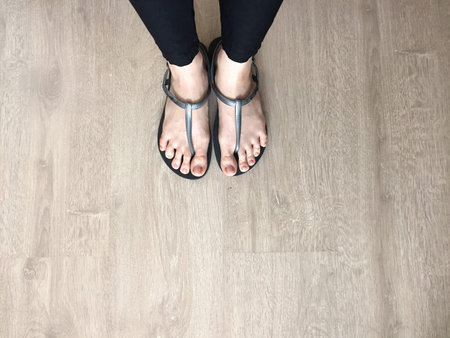 Close Up on Woman's Feet Wearing Black Sandals and Black Jeans on Wooden Background Great For Any...