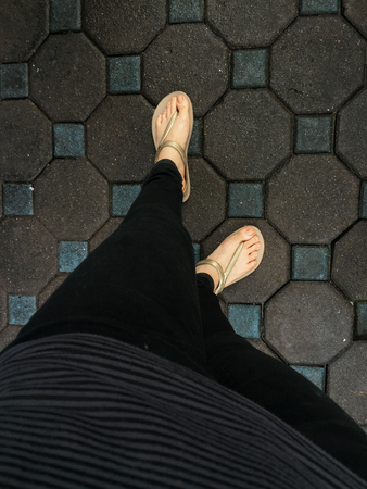 Selfie Woman's Feet Wearing Sandals and Black Jeans on Tile Background Great For Any Use.の写真素材