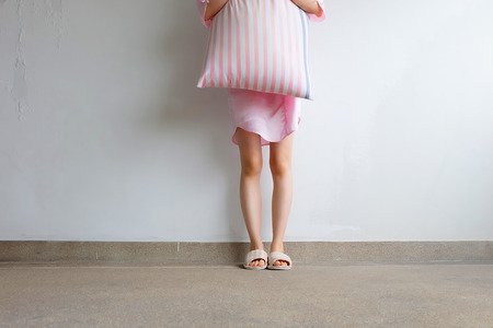 Girl Standing in Sleepwear and Pink Checkered Slippers with Holding Pink Pillow on Floor Background Great for Any Use.の写真素材