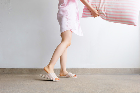 Girl Standing in Sleepwear and Pink Checkered Slippers with Holding Pink Pillow on Floor Background Great for Any Use.の写真素材