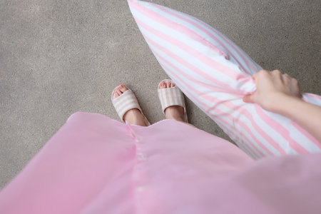 Girl Standing in Sleepwear and Pink Checkered Slippers with Holding Pink Pillow on Floor Background Great for Any Use.の写真素材