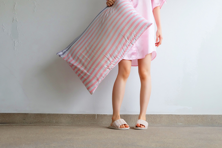 Girl Standing in Sleepwear and Pink Checkered Slippers with Holding Pink Pillow on Floor Background Great for Any Use.の写真素材