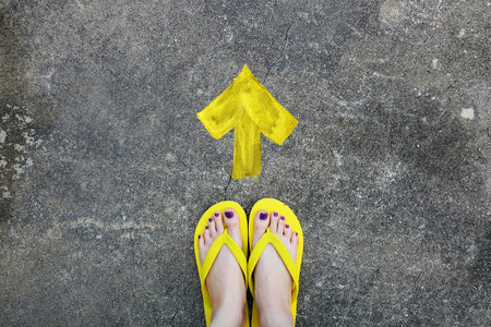 Yellow Arrows Direction. Womanâs Sandals Feet with Violet Nail Pedicure on Cement Background Great for Any Use.の写真素材