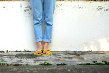 Yellow Sandals. Woman Wearing Flip Flops and Blue Jeans Standing on Old Cement Floor Background Great for Any Use.の写真素材
