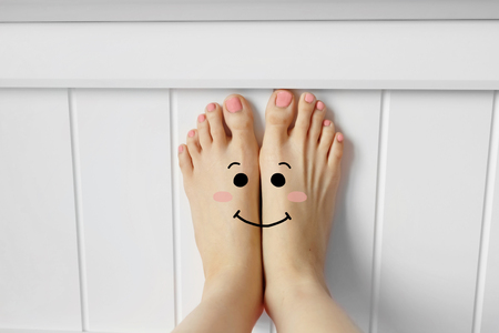 Smiley Face Barefoot with Pink Nail Polish Manicure. Beautiful Female Feet with White Headboard Bedroom Background Great for Any Use.の写真素材