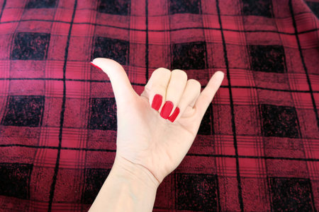 Beauty Red Manicure Nail with Gel Polish. Woman Hand with Red Nails on the Red Scot Fabric...