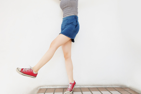 Red Sneakers of Free Space. Beautiful Slim Woman Legs with Red Shoes and Jean Skirt on Floor Background Great for Any Use.の写真素材