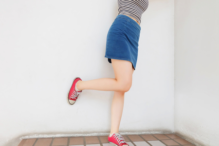 Red Sneakers of Free Space. Beautiful Slim Woman Legs with Red Shoes and Jean Skirt on Floor Background Great for Any Use.の写真素材