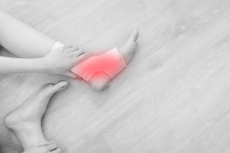 Closeup of a Foot with Gauze Elastic Bandage. Asian Woman Ankle Injury Runner. Hands on Injured Legs and Feet with Red Spot on Pain Area Sitting on a Wooden Floor Background from Rupture or Tear.の写真素材