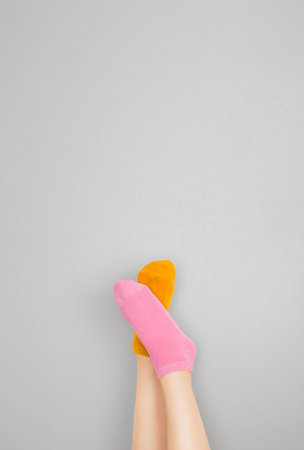 Legs and feet with cute sock. Woman wearing pastel pink and yellow socks raised crossed leg isolated on gray background. Top view. Beauty and fashion concept. Minimalism fashionable winter set.の写真素材
