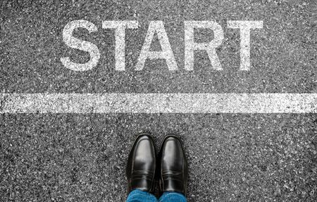 Business man standing on grunge concrete with white race line beginning idea. Top view. Feet and black shoes with word start written for concept on tarmac road background. Businessman challenge.の写真素材