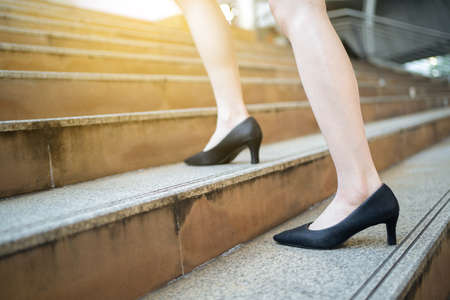 Leg of businesswoman on black high heels shoes. Young adult woman is walk step up on the street stairs outdoor background. City business progress concept design.の写真素材