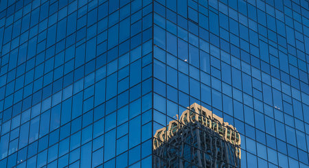 A striking view of a modern building with a blue glass facade, reflecting another building, showcasing contemporary architecture and urban design.の素材