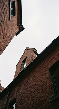 Low angle shot of brick buildings with dark roofs against a cloudy sky. The image captures the architectural details and textures of the buildings.の素材