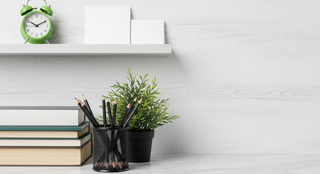 A well-organized desk with books, pencils, a small plant, and a clock on a shelf, creating a clean and functional workspace.の素材