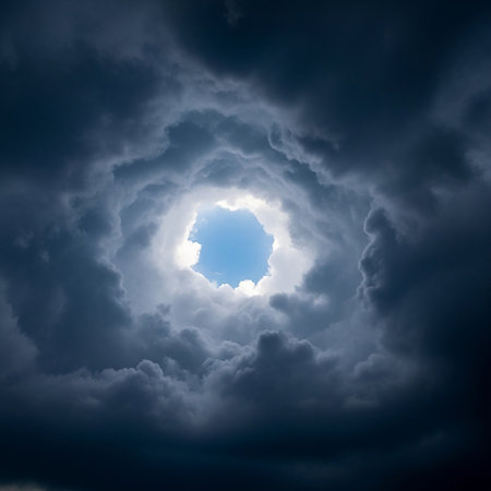 A striking view of a circular opening in dark, turbulent storm clouds, revealing a bright, clear blue sky within.の素材