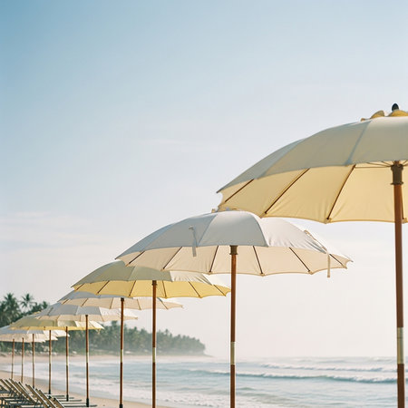 A tranquil beach setting featuring a neat row of light-colored umbrellas extending along the shore, with gentle ocean waves in the background and a clear, bright sky overhead, evoking a sense of calm and relaxation.の素材